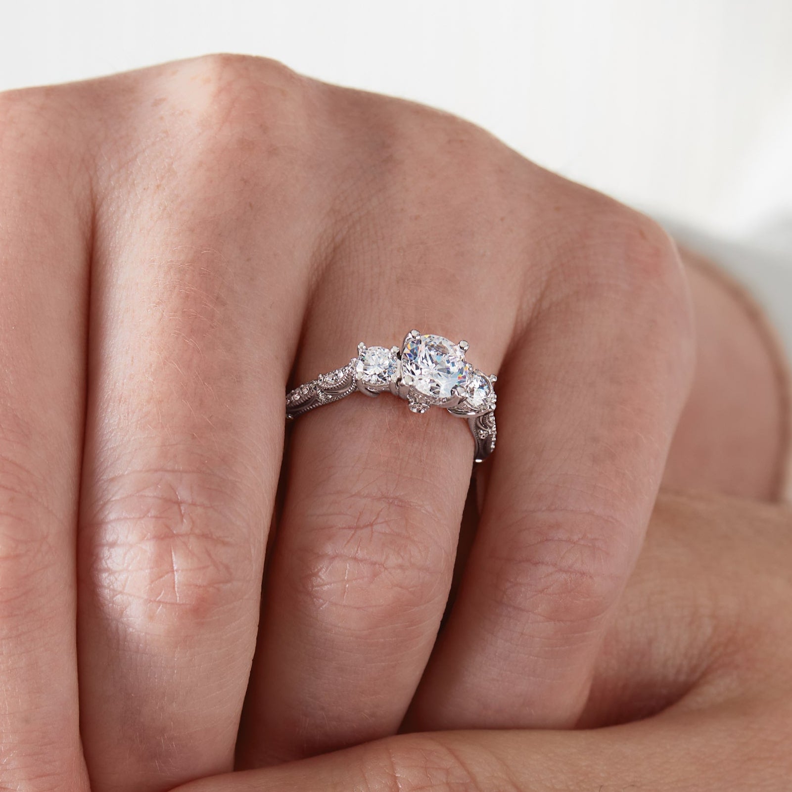 Close-up of a hand wearing a diamond ring on a light background 3 stone engagement ring