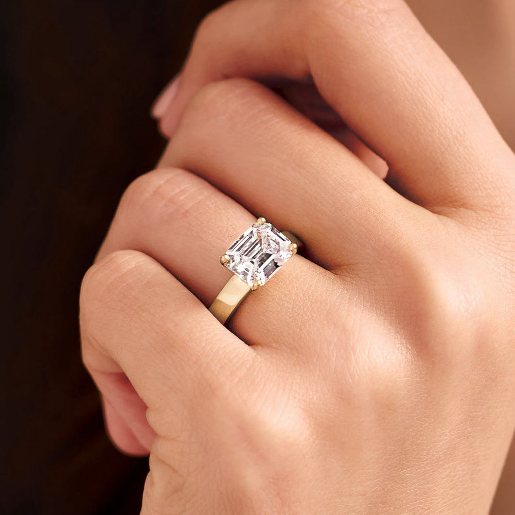 Close-up of a hand wearing a solitaire diamond engagement ring with a blurred background