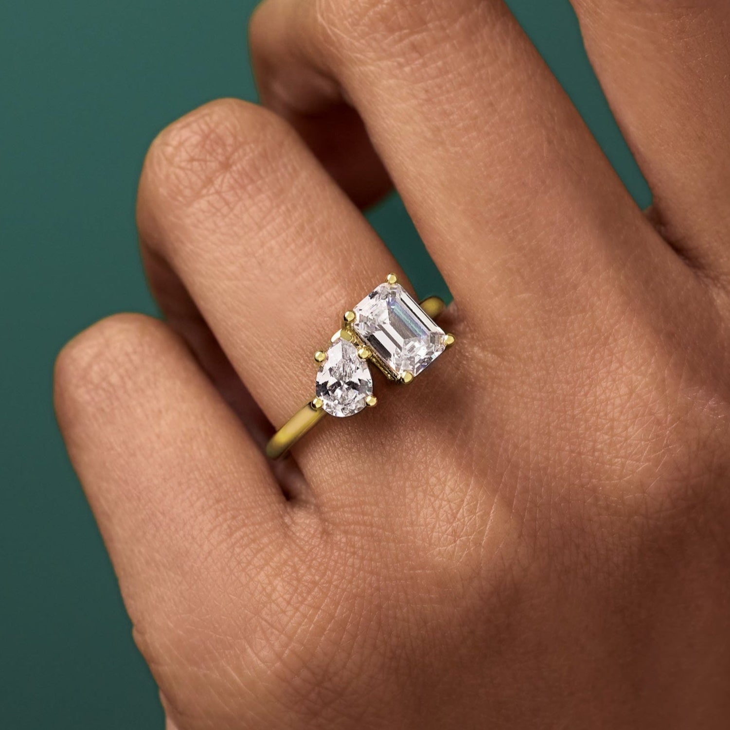 Two Stone engagement ring with two diamonds on a hand against a green background